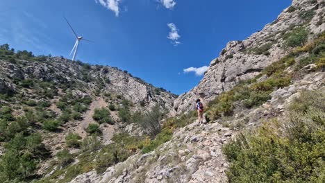 Fit-young-woman-climbing-a-rocky-mountain-with-a-windmill-in-background