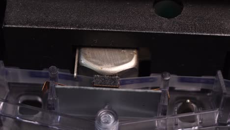 cinta de cassette de audio que se mueve bajo la cabeza magnética en un reproductor de cubiertas vintage, comenzando la reproducción o la grabación