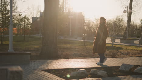 a girl wearing a brown coat, hoodie, jeans, and white shoes wanders through a quiet park during sunset, looking saddening. the warm, golden light casts long shadows, adding a reflective atmosphere