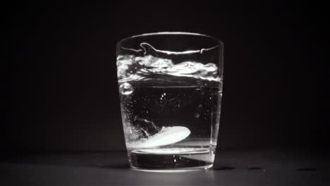 tablet falls to the bottom of the glass with water a black background slow motion