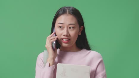 아시아 여학생이 녹색 스크린 스튜디오에서 휴대전화로 이야기하고 있습니다.