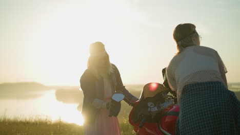 two friends are meticulously cleaning a red power bike in a serene grassy field, one focuses on wiping the glass, while the other cleans the tank