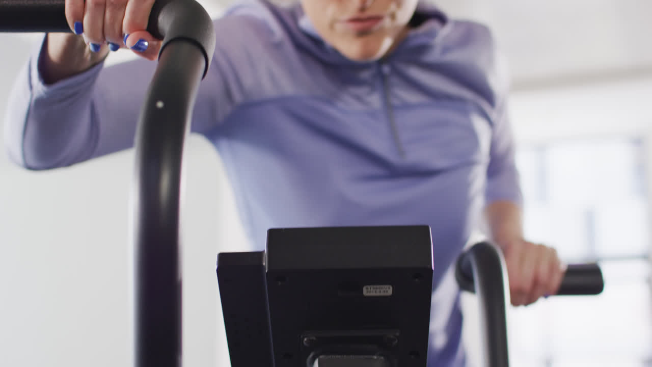 Video portrait of determined caucasian woman on exercise bike working out at a gym