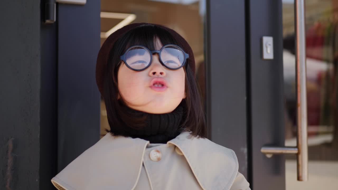 chica coreana en un abrigo gris y gorra se encuentra en la calle en primavera en las puertas de vidrio de la tienda