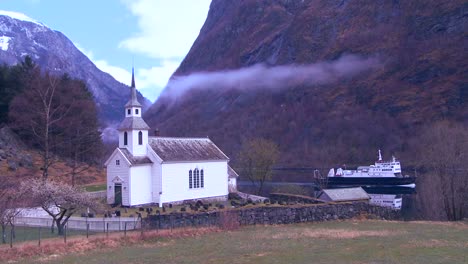 a ferry boat passes a pretty church along the shore in norway