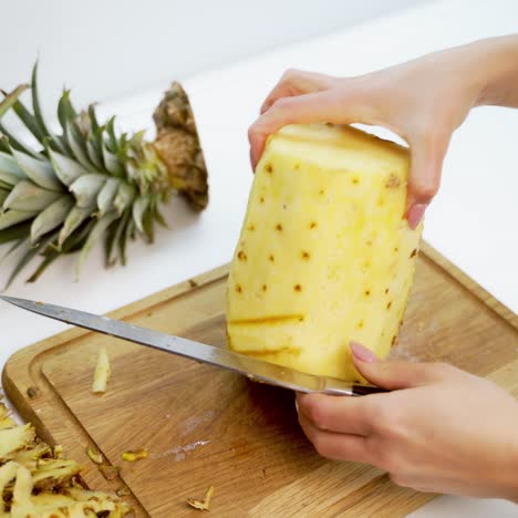 fresh peeled pineapple on a wooden board. woman's hands holding sharp knife and cleaning pineapple on the table.