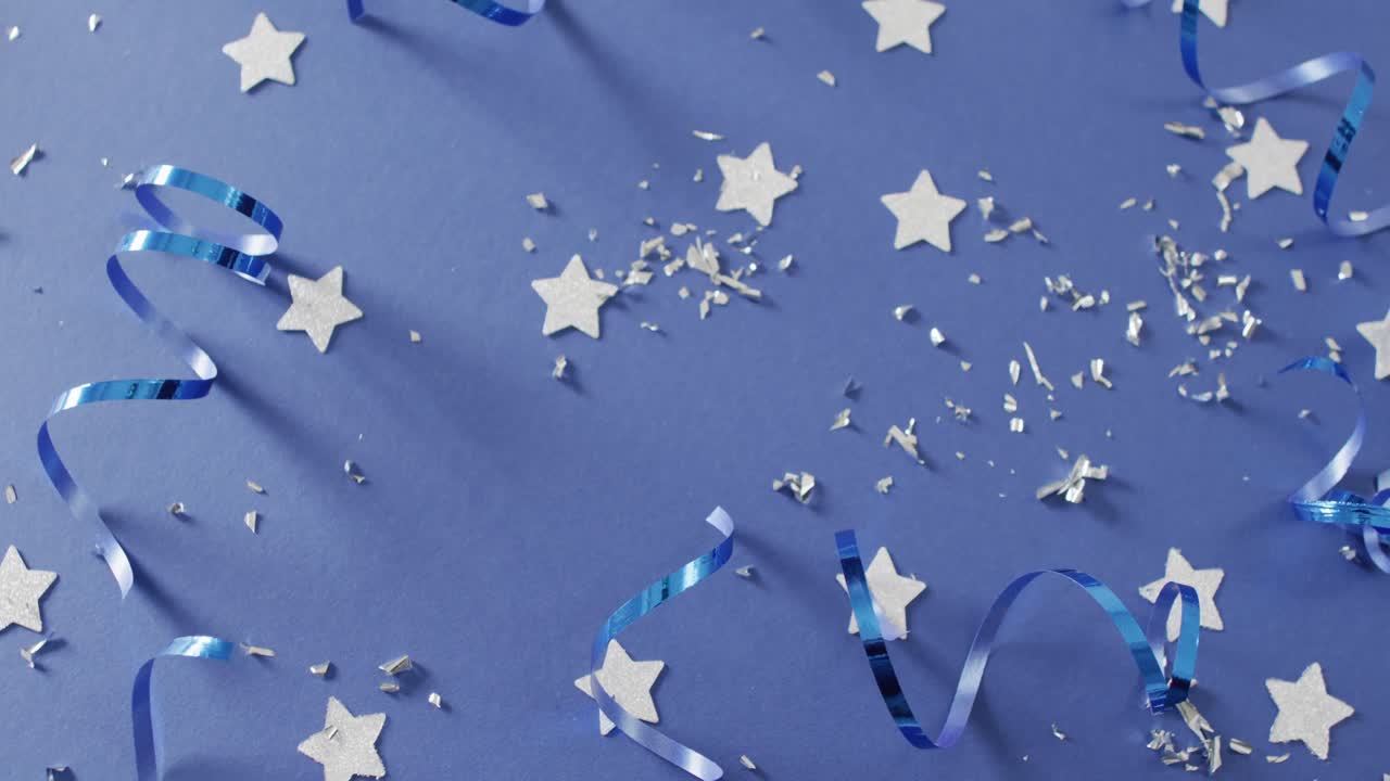 파란색 배경에  ⁇ 어져 있는 여러 개의 은색 별과 파티 스트리머의 비디오