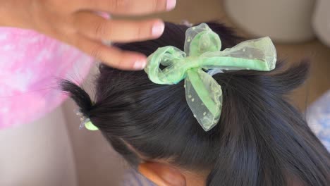 mother styling daughter's hair with a green bow