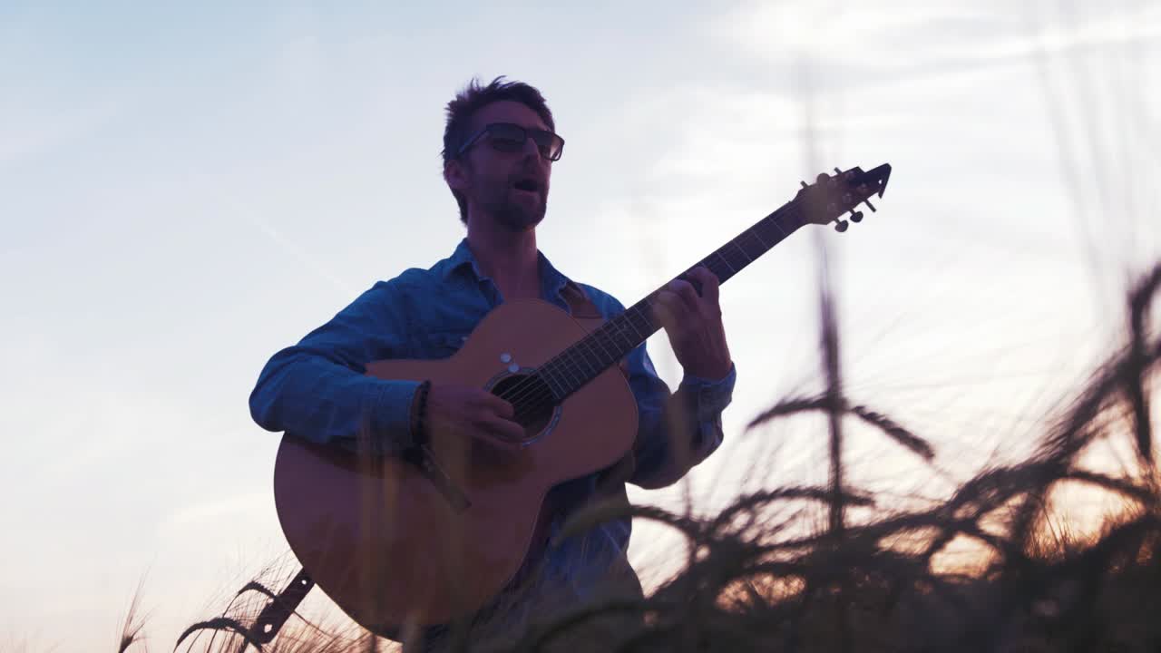 Musiker spielt Gitarre bei Sonnenuntergang im Weizenfeld.