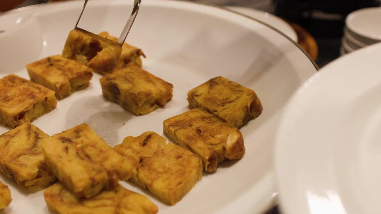 Pinze di metallo afferrano pezzi quadrati di omelette thailandese da un piatto da buffet bianco in un ristorante