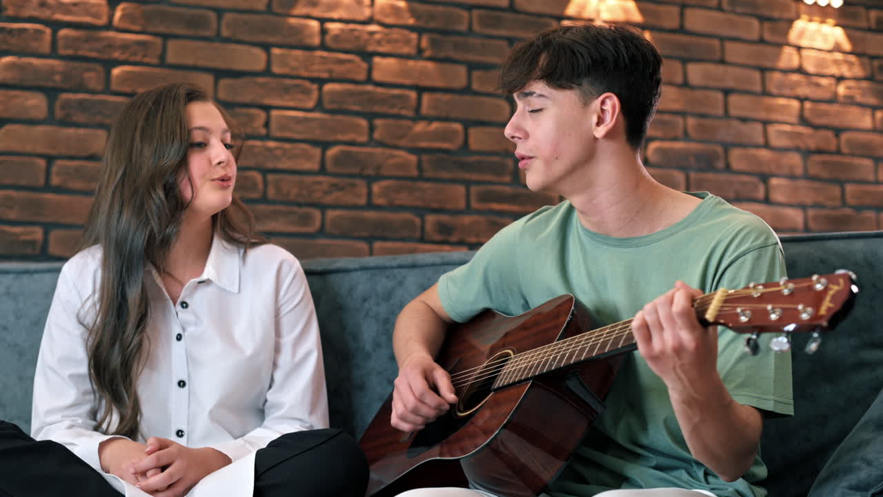 Young man and woman playing on a guitar and singing, looking at each other