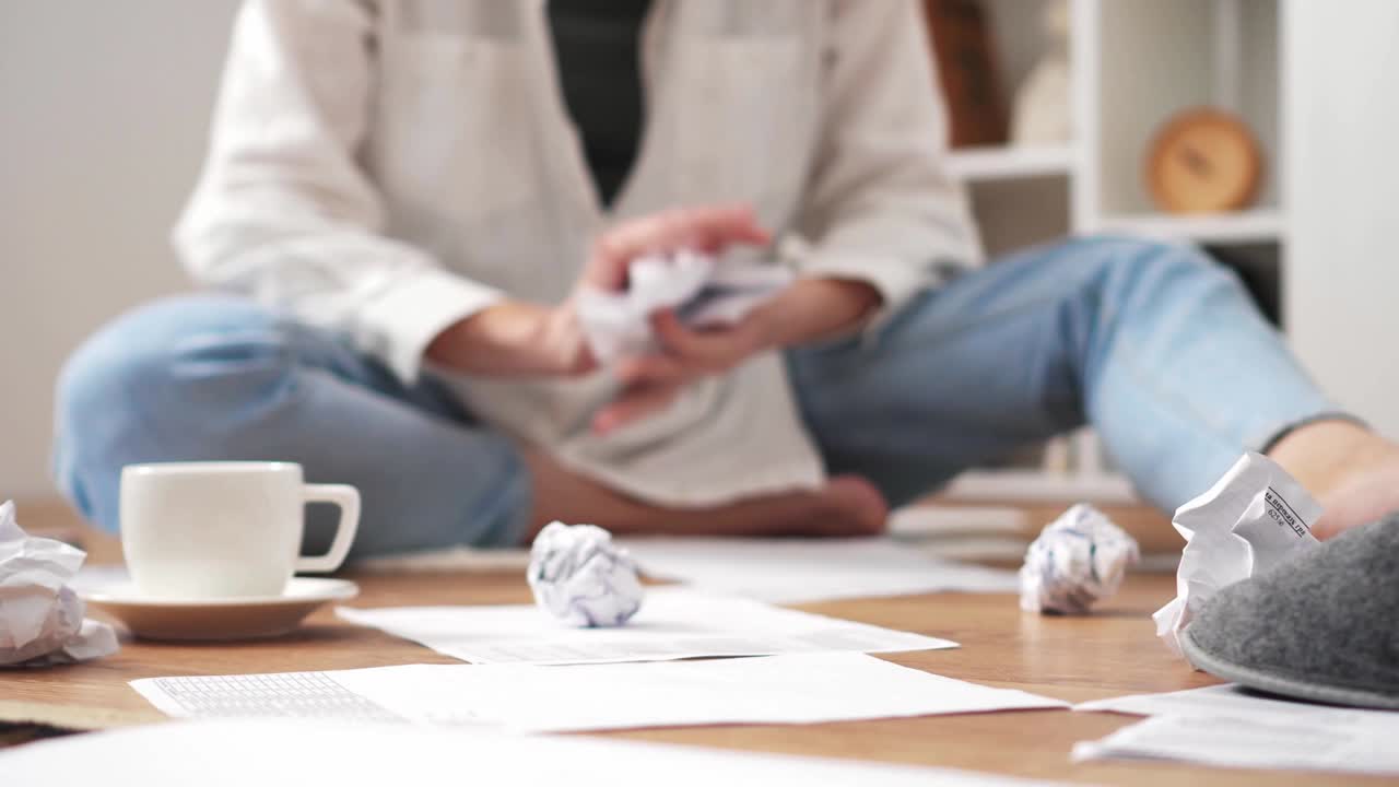 la chica está sentada en el suelo trabajando revisando estudiando el informe. la mano lanza el papel