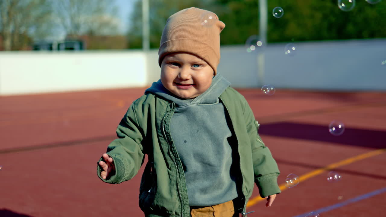 Little two-year-old boy on a walk on the street. Boy in a jacket and sneakers, children's stylish clothes. Toddler in a light hat on a walk