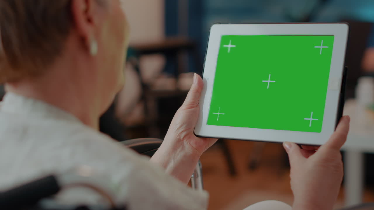 초록색 화면을 가진 태블릿을 사용하는 고령 여성