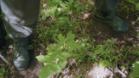 warrior lifting right leg in swinging motion while left leg supports on soft loamy grass ground under forest canopy sunlight casting dappled shadows conveying dynamic tactical movement