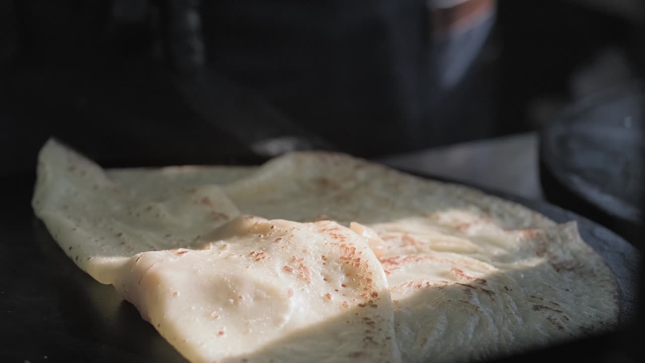 vista lateral de la cocción de un panqueque ruso en una sartén profesional. el chef vierte la masa en la sartén y envuelve los hongos y el queso en un pancake horneado