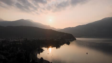 Vista-Aérea-Del-Amanecer-Mágico-Sobre-El-Lago-De-Garda-Y-La-Ciudad-De-Riva-Del-Garda-Junto-Al-Lago-En-La-Mañana-De-Verano,-Disparo-De-Drones