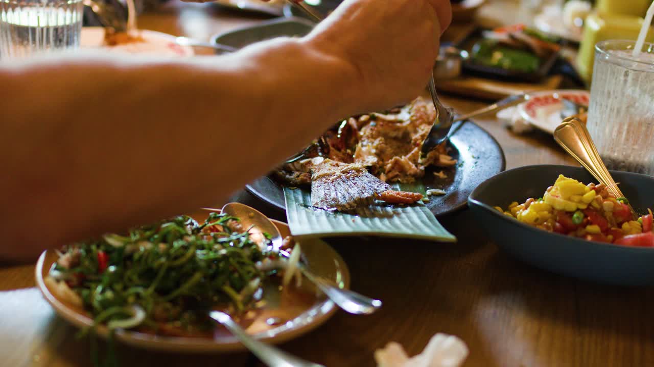 Diners enjoy authentic Thai grilled fish and spicy salad in warm, natural restaurant lighting