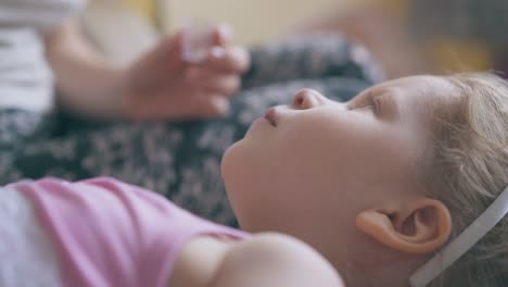 mother gives nose drops to unhappy girl on soft bed closeup