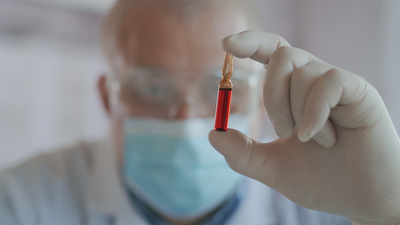 un científico masculino sostiene una ampolla de vidrio rojo con una vacuna y la mira de cerca en cámara lenta. vacunas. imágenes de alta calidad en 4k