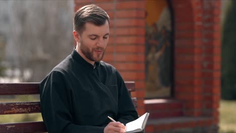 a cute smiling priest writes down his thoughts in a notebook