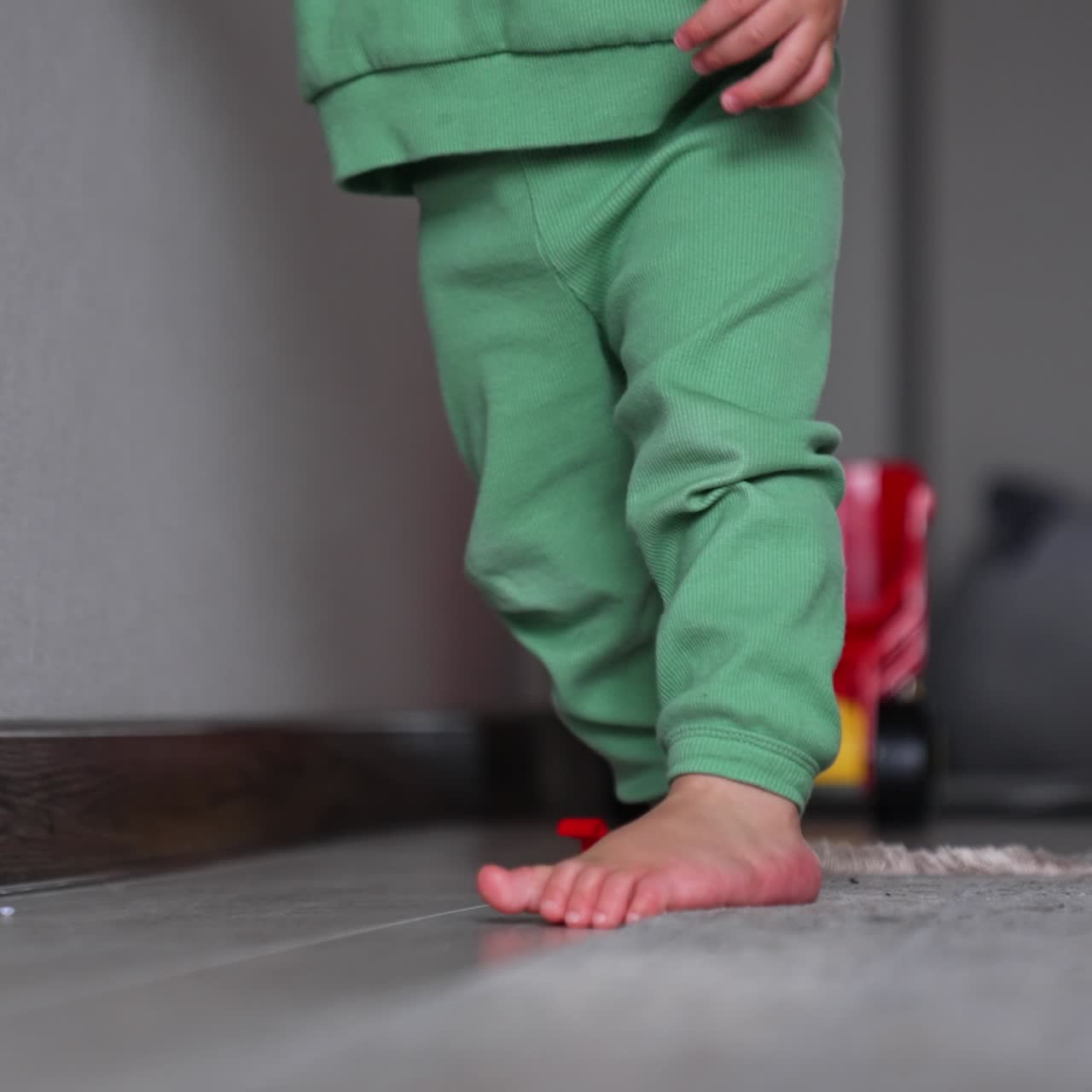 Bare little feet of a toddler standing on the floor. One year old child learns to stand leaning on the wall