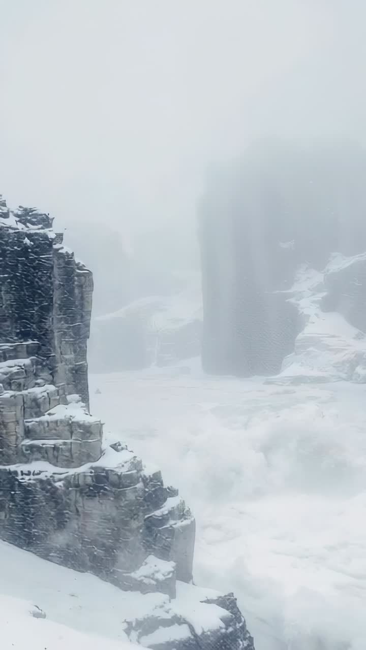 Vertical video: Panning camera revealing right rock column in snowy gorge, with fog thinning