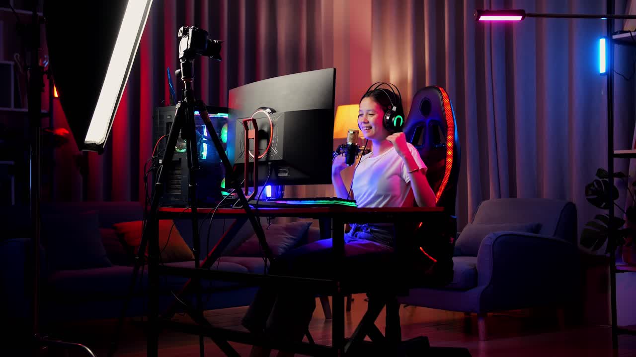 asian girl streamer gritando gol y bailando celebrando el juego ganador a través de la red en la computadora personal. videojuego de transmisión en vivo, escritorio iluminado por luz de tira de led rgb