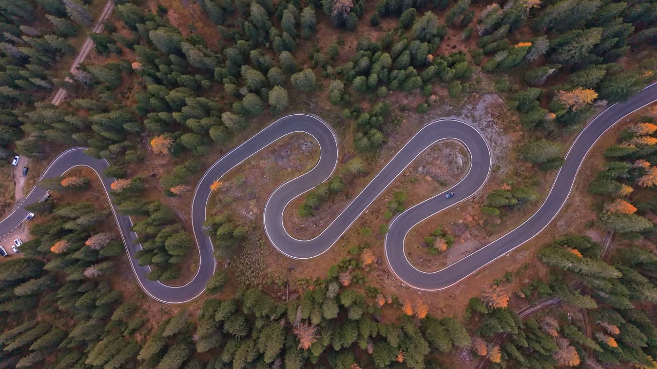 Snake-like mountain road through golden trees, Dolomites aerial view