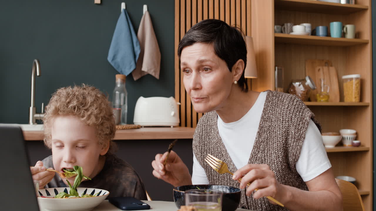 Mother and Son Eating a Meal at Home with a Laptop