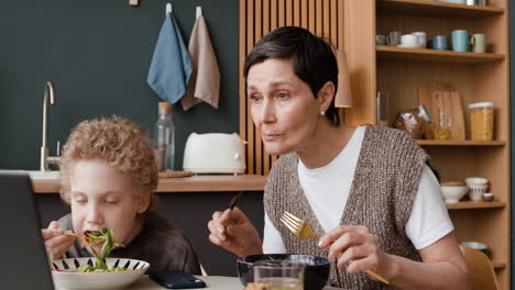 mother and son eating a meal at home with a laptop