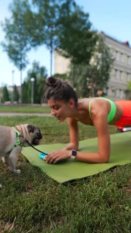 woman doing plank exercise in park with a pug dog