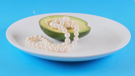 medio aguacate fresco con perlas en un plato blanco cubierto de guiones sobre un fondo azul claro