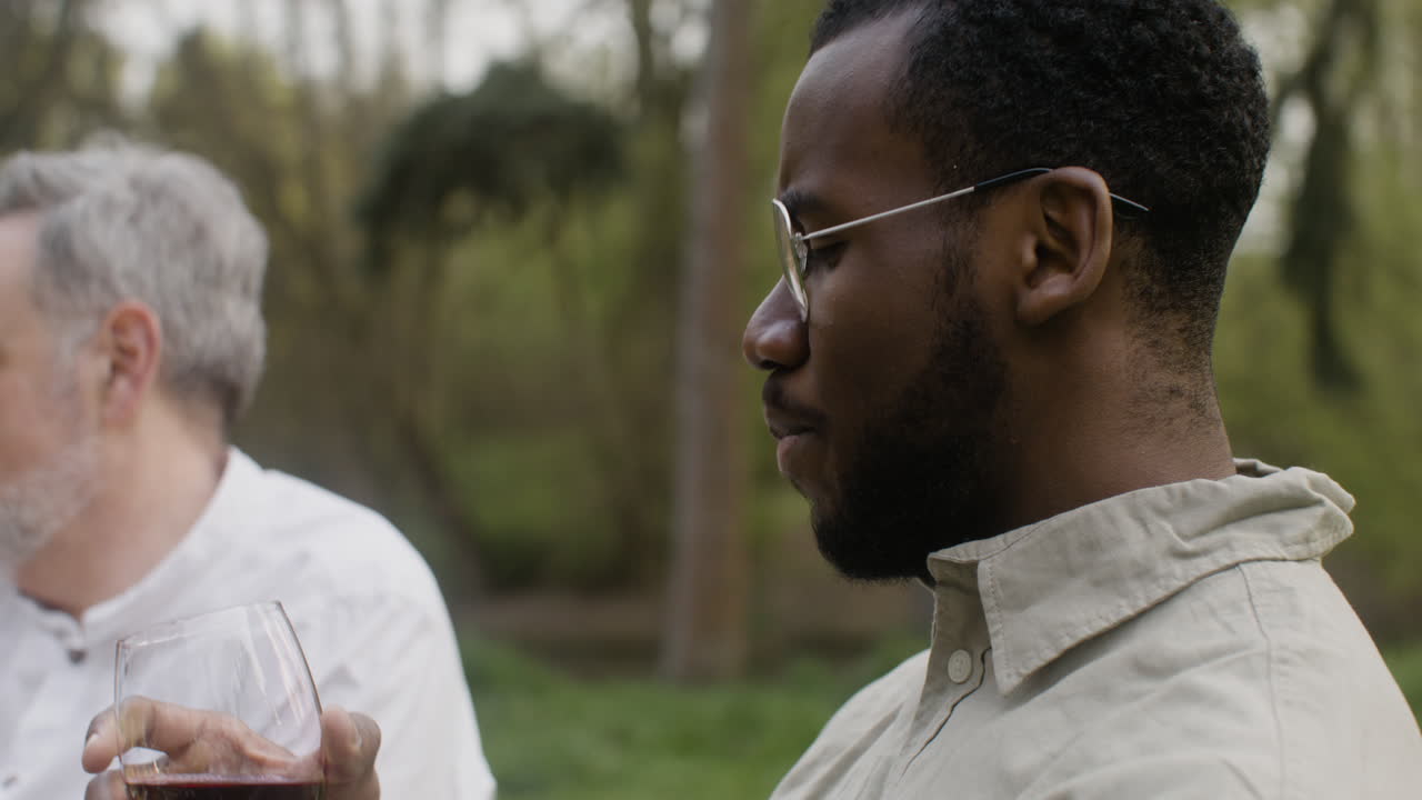 vista de cerca de un hombre bebiendo vino tinto mientras se sienta a la mesa durante una fiesta al aire libre en el parque