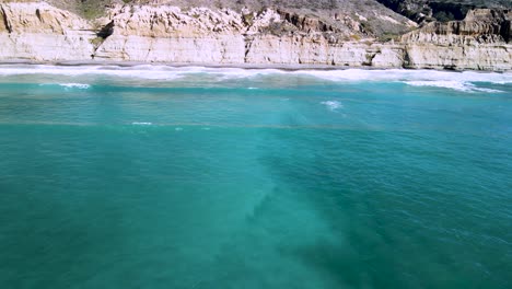 Aerial-pan-across-white-eroded-cliffs-and-beauitufl-green-ocean-water-as-waves-crash-over-reef