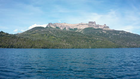 low forward aerial over lake by forested mountains in argentina