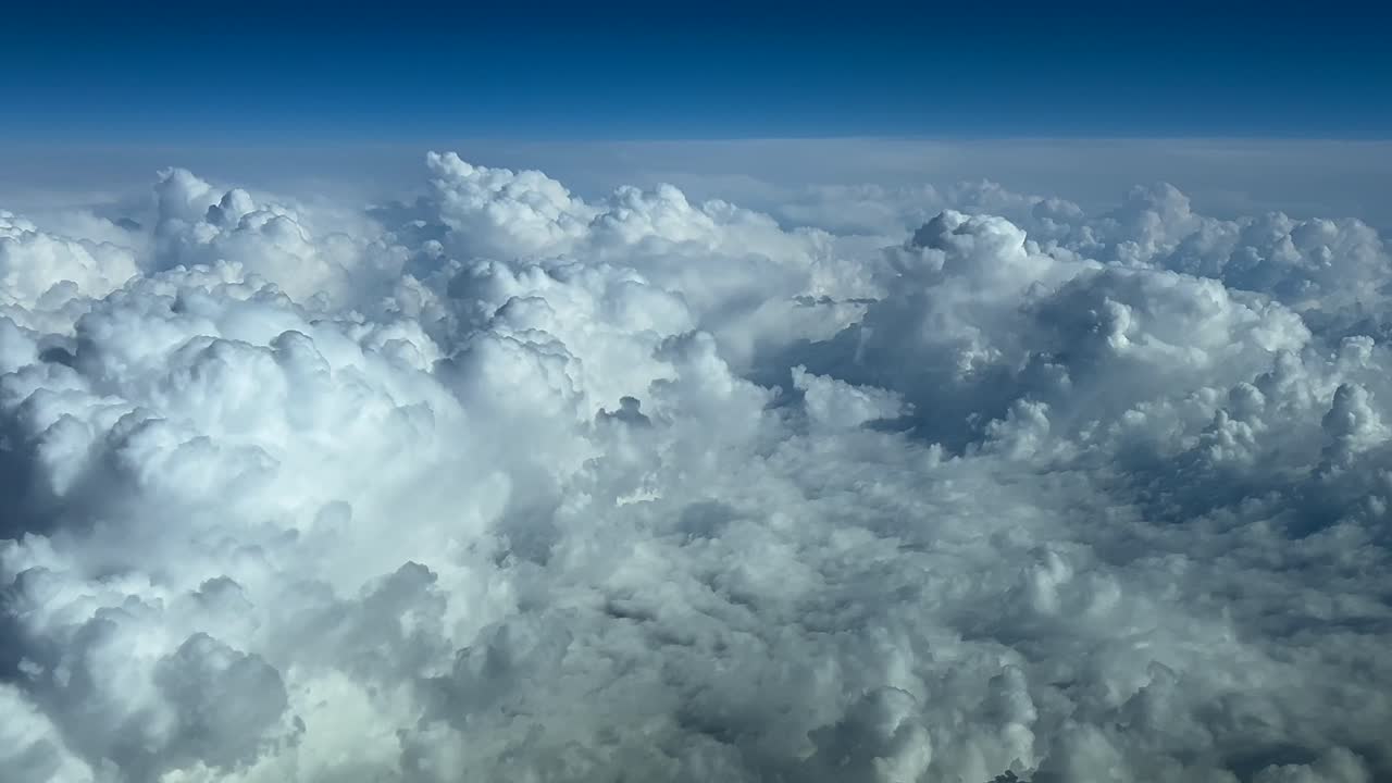 Storm clouds in a blue sky seen from above. Immersive pilot POV shot from a jet cockpit at cruise level FL300. 4K 60FPS