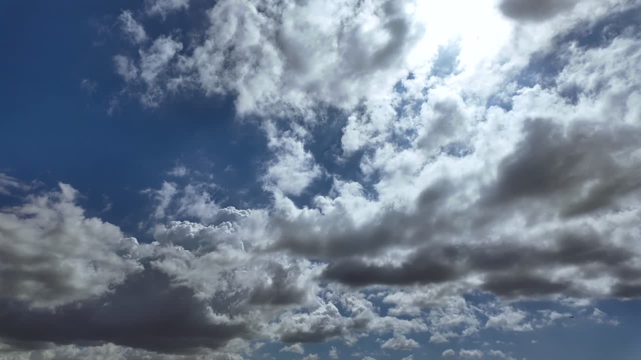 Timelapse of cottony storm clouds evolving in a blue sky, with a radiant sun veiled by a layer of ethereal clouds