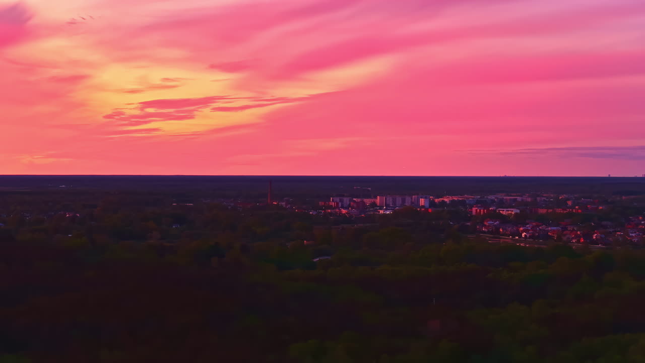 Pink sunset over cityscape under dramatic sky, drone video