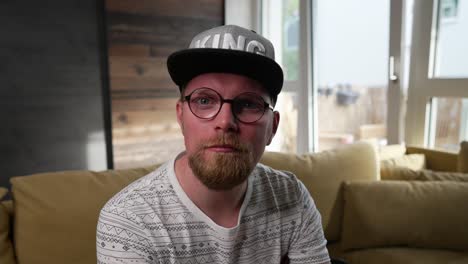 man with glasses and cap looks at camera with a serious, stern look, medium shot