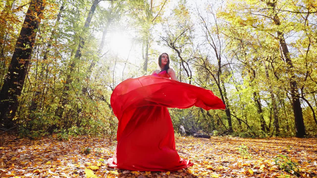 A Captivating Dance of Color: A Woman in a Flowing Red Dress Elegantly Moves Amidst Autumn's Golden Foliage, Celebrating Nature's Beauty and Grace