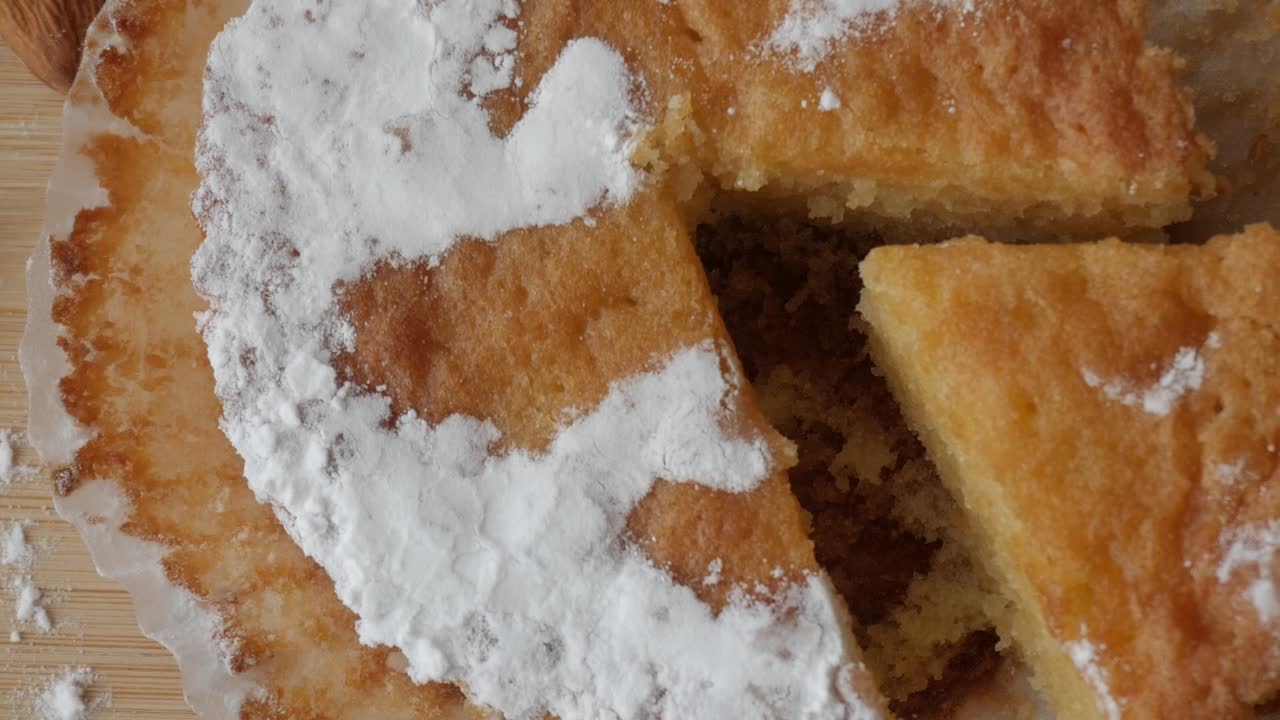 Pan right view of a traditional Tarta de Santiago with powdered sugar cross and almonds on a wooden table