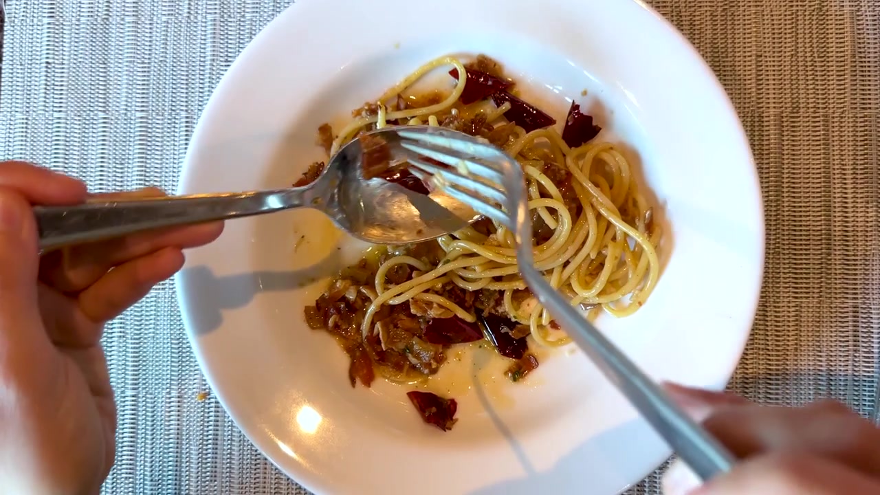 Ripresa dall'alto di mani che mangiano spaghetti con peperoncino e pancetta