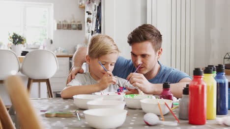 Padre-Con-Hijo-Sentado-A-La-Mesa-Decorando-Huevos-De-Pascua-En-Casa