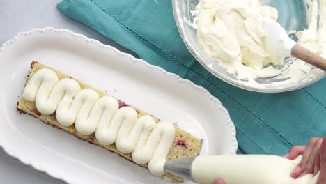making a dessert called red raspberry tea cake made with fresh berries and vanilla buttercream frosting. great for tea parties. piping and decorating the top of the vanilla cake with fresh berries