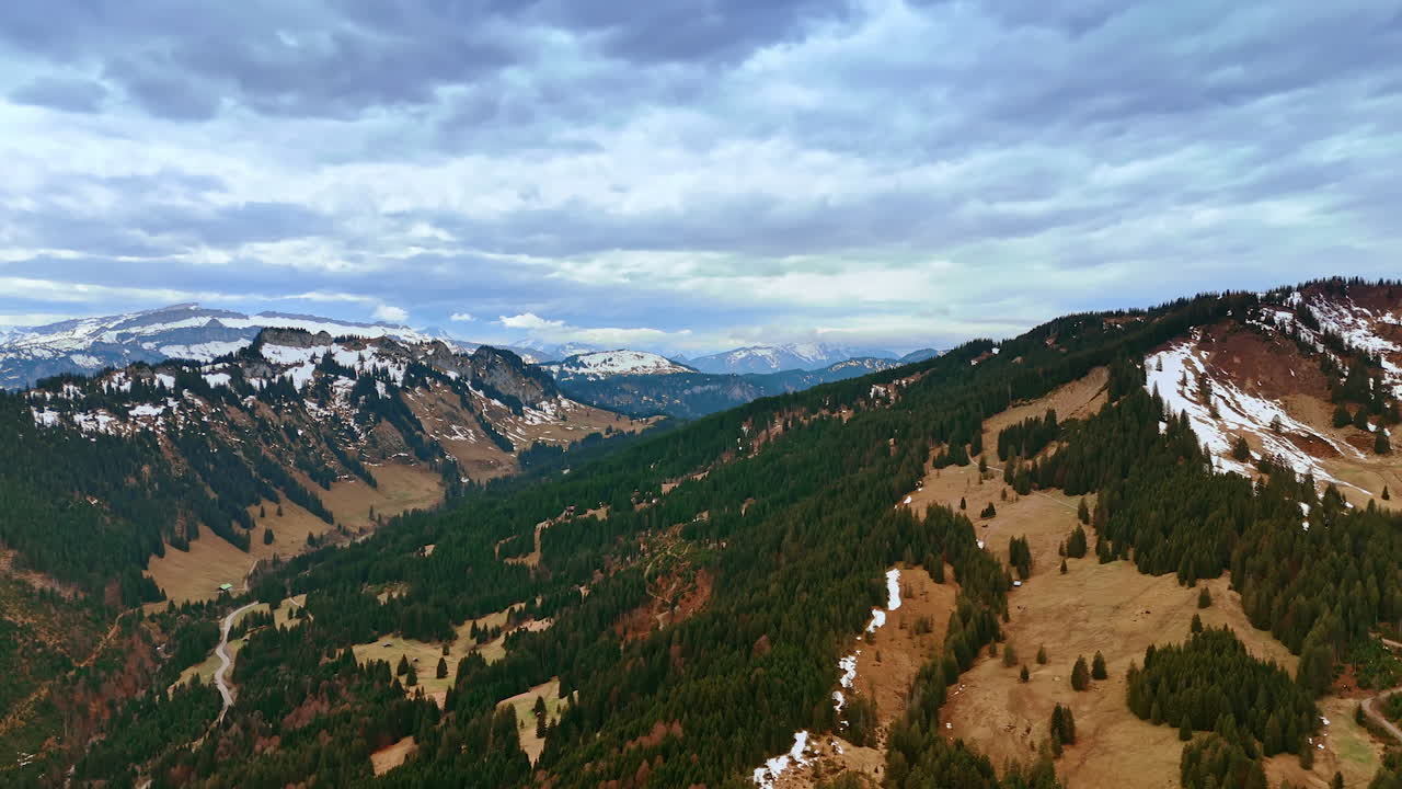 Thick grey cloudscape hanging over the mountain tops. Drone flight over the rocks covered with evergreen woods and some snow.