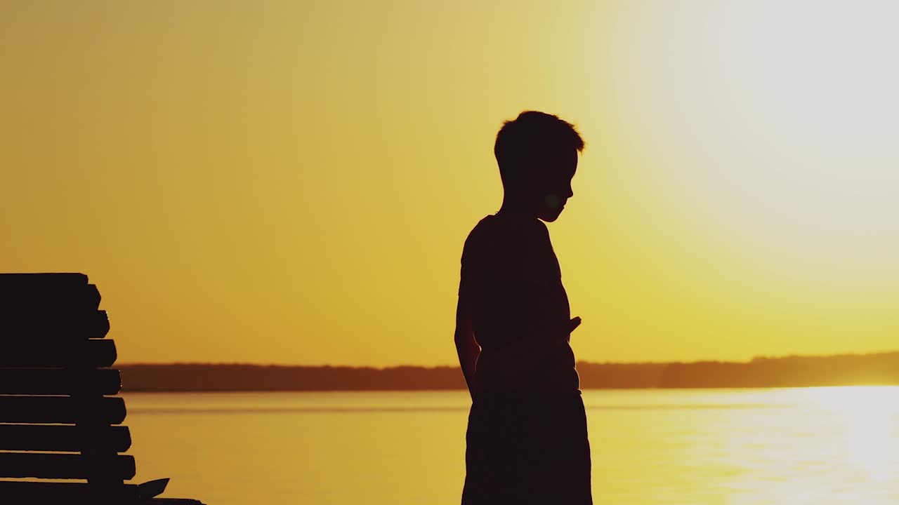 little kid holds origami of paper airplane in his hand and plays at sunset on the background of lake. A boy passionates about playing with his paper toy