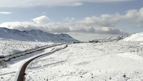 Snowy-mountain-traffic-aerial-descending-view-down-to-road-leading-to-congested-traffic-road