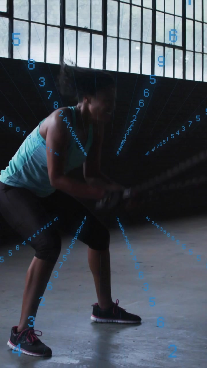 Woman doing battle-rope in warehouse gripping rope, driving waves as blue numbers tracking fitness