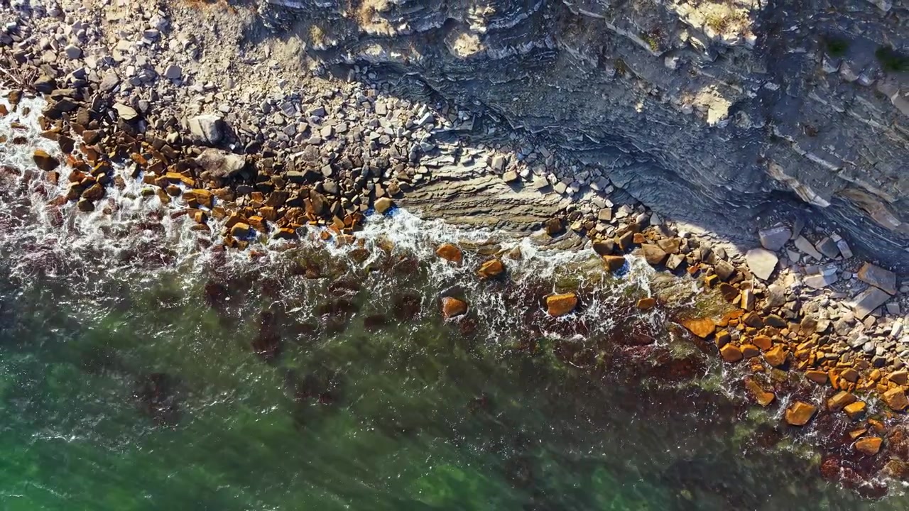 Le onde si infrangono sulla costa rocciosa con acqua verde e limpida in una giornata di sole.